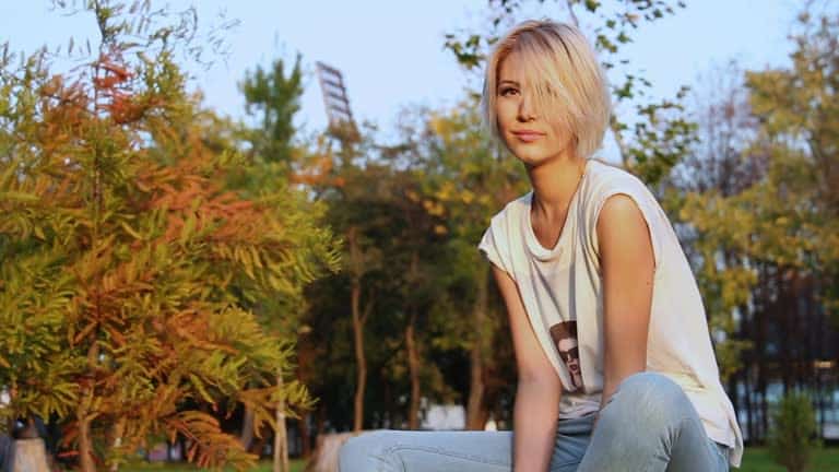 stylish young blonde woman posing on a tree stump in autumn park.